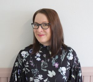 Tummatukkainen, silmälasipäinen nainen värikkäässä puserossa