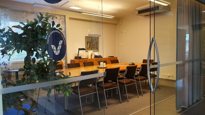 Kokoustilakuva, jossa näkyy tuoleja ja pitkä pöytä kera viherkasvien