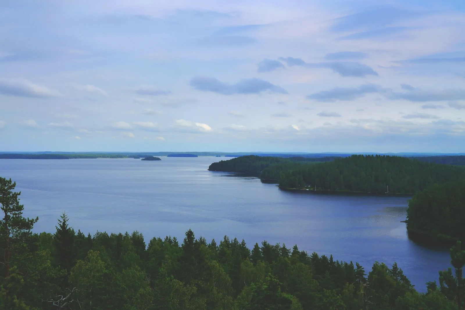 Suomalainen järvimaisema, kaukana siintävä metsäinen ranta ja pilvistä taivasta