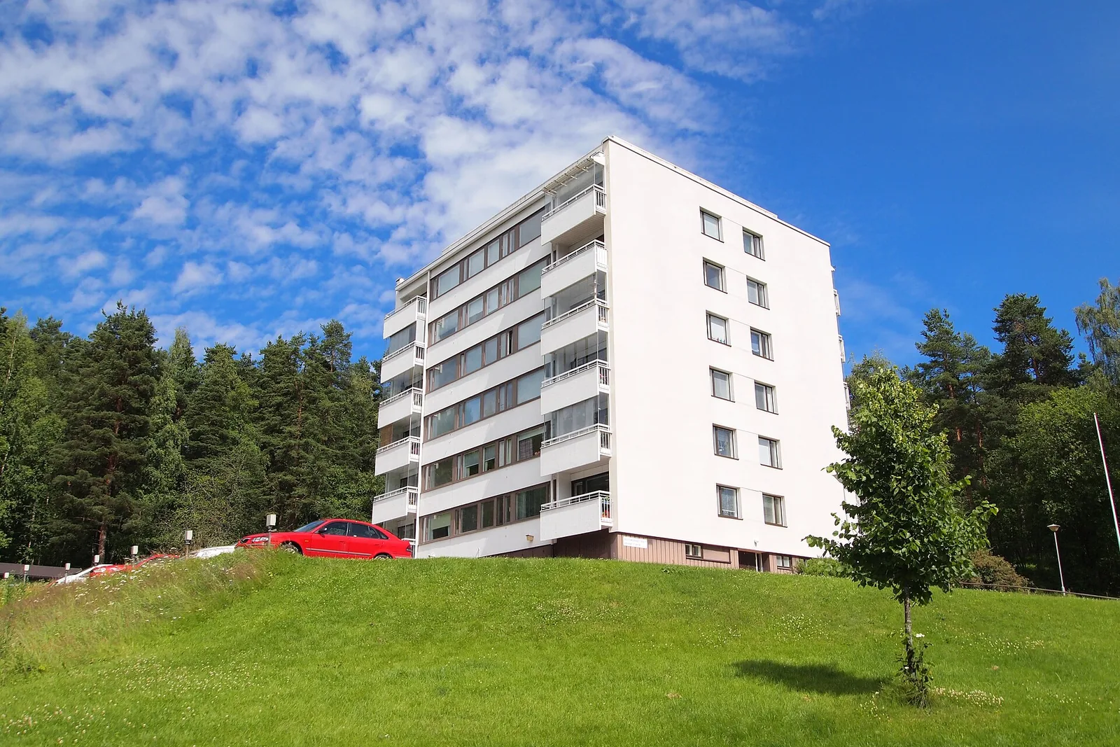 Valkoinen kerrostalo nurmikkoisen rinteen päällä kesäpäivänä
