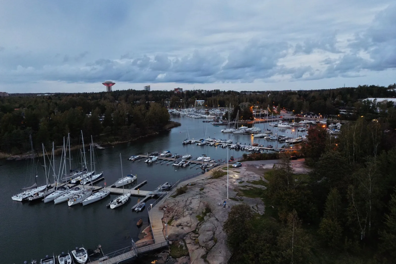 Ilmakuva veneillä täytetystä satamasta metsäisen rannan äärellä