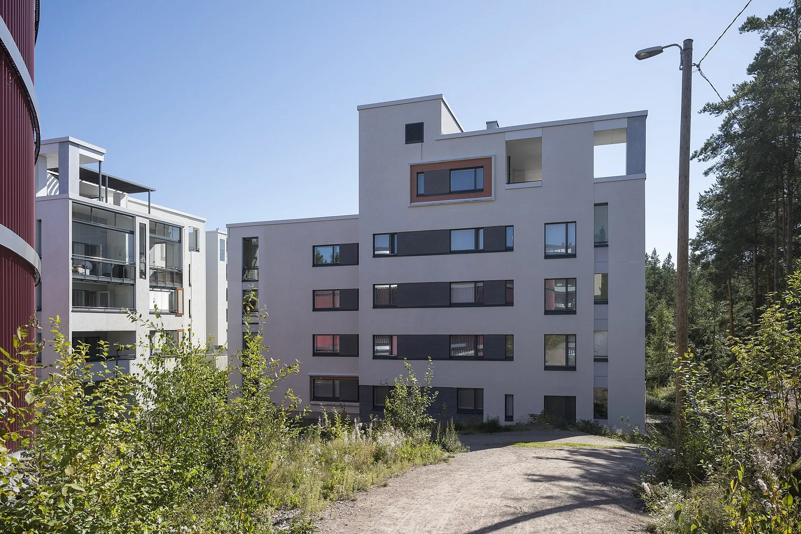 Vaalea kerrostalo metsän reunassa kesäpäivänä