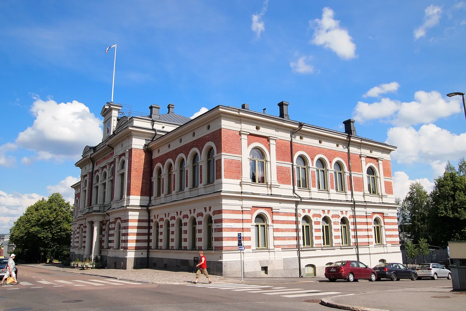 Punavalkoraidallinen kaupungintalo kadunkulmassa sinistä taivasta vasten