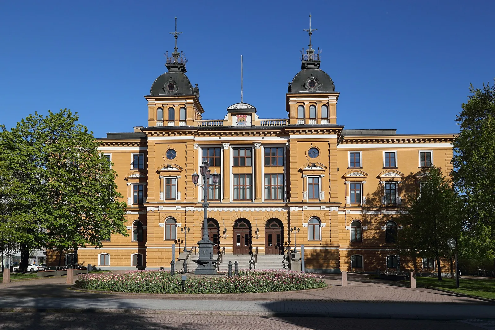 Keltainen kaksitorninen kaupungintalo puiden reunustamana